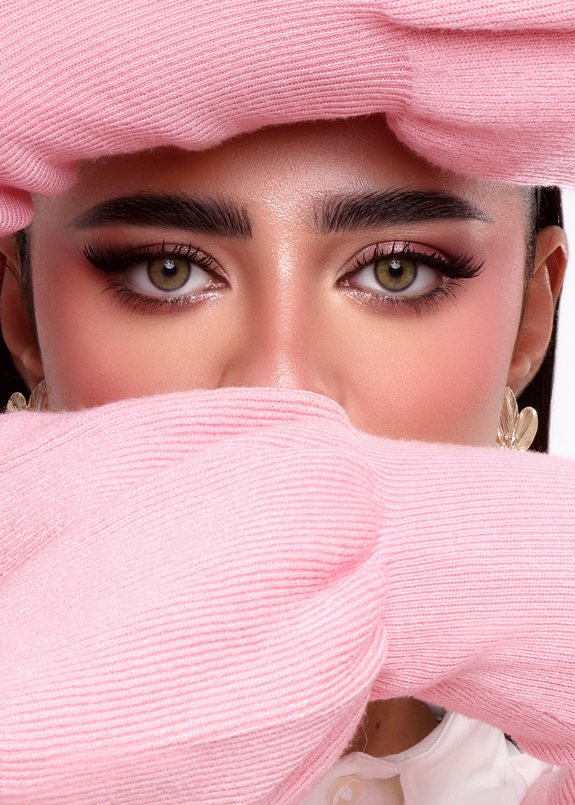 Person wearing a pink headscarf and covering their mouth with it, with a white background.